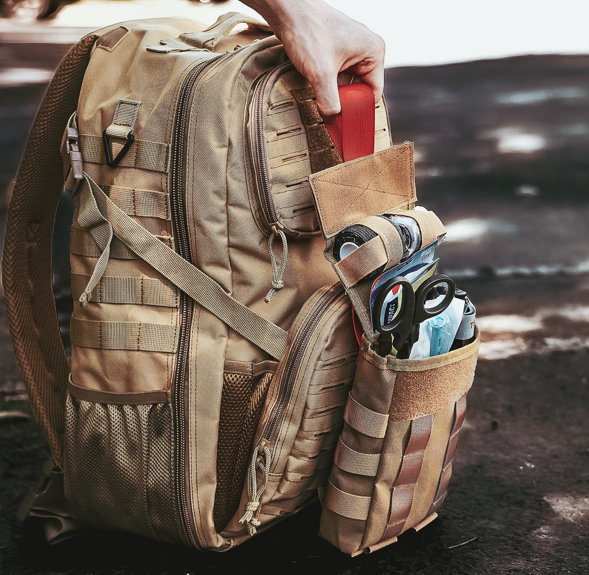 Fully stocked tan tactical IFAK pouch attached to MOLLE backpack, displaying trauma shears, QuikClot gauze, and emergency medical gear ready for rapid deployment.