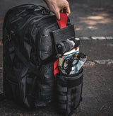Fully stocked black tactical IFAK pouch attached to MOLLE backpack, displaying trauma shears, QuikClot gauze, and emergency medical gear ready for rapid deployment.