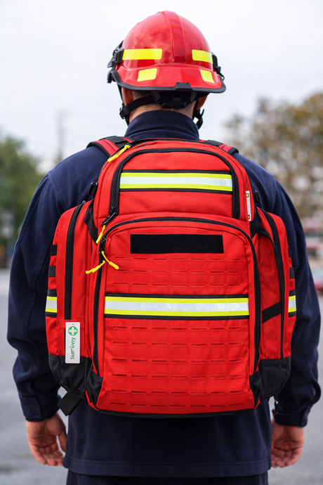 Person wearing a red emergency backpack with reflective stripes, outdoors.